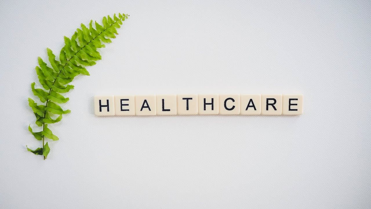 Services-01 Healthcare word spelled with Scrabble tiles next to a green fern leaf on a white background.