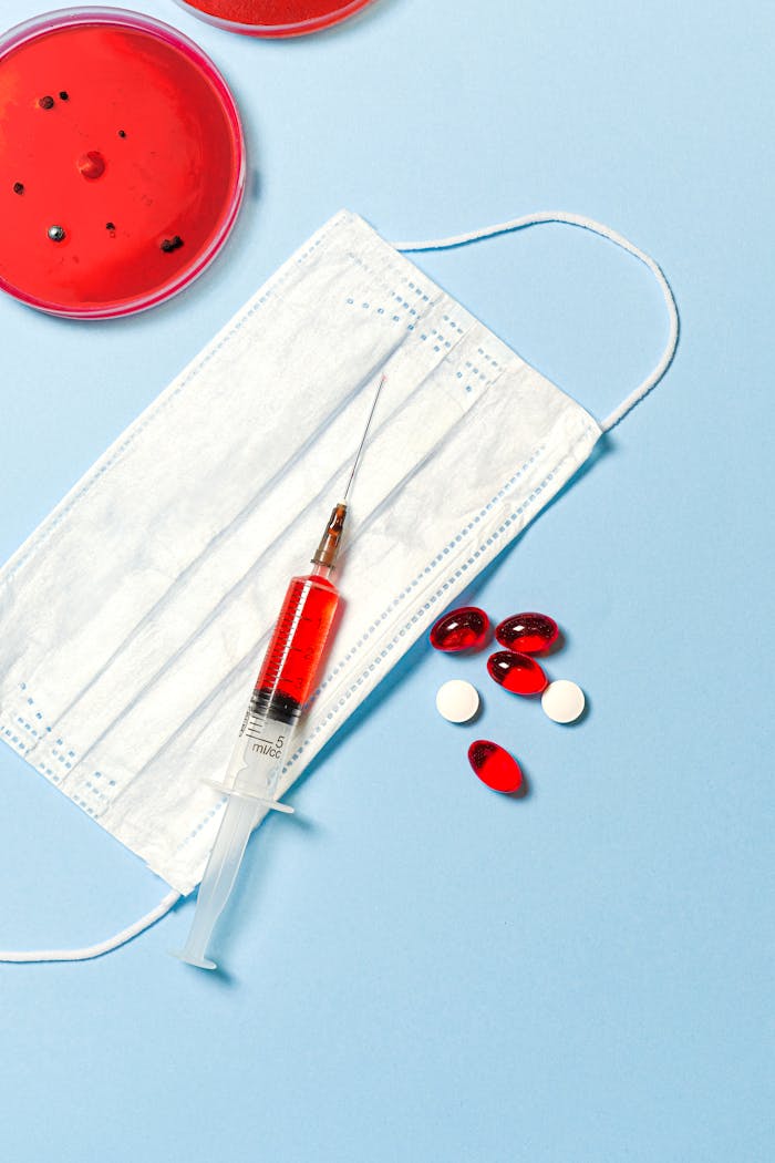 creative Face mask, syringe, and pills on a blue background, symbolizing healthcare and medical research.
