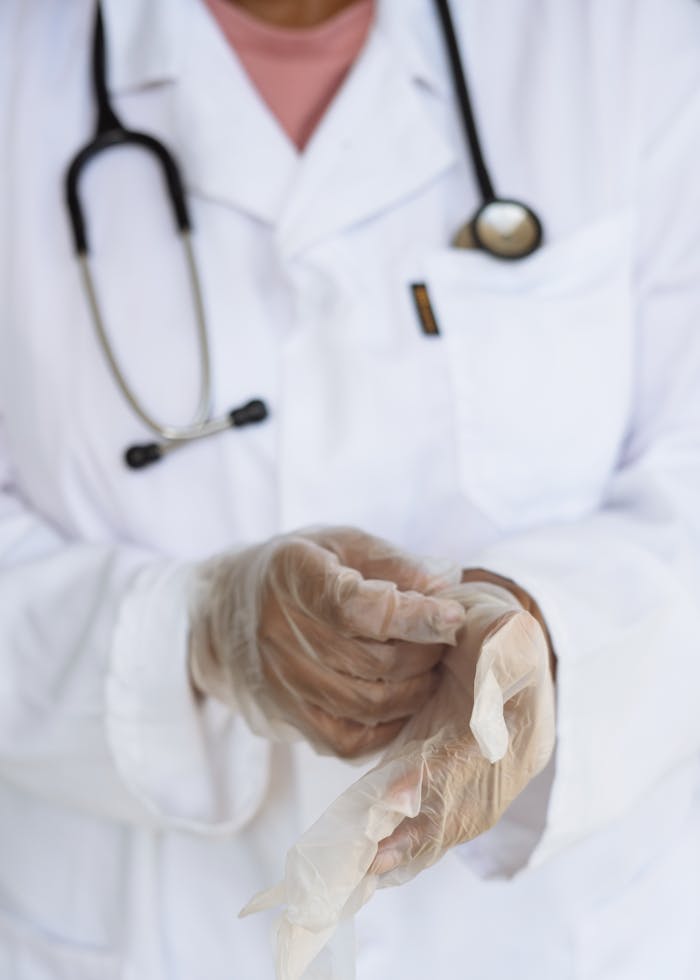 Services-03 Faceless ethnic medical worker in lab coat and stethoscope taking of transparent gloves after approaching patients for examination in modern hospital